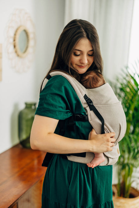A mother wearing a LennyLight baby carrier in Peanut Butter color, comfortably holding her baby while smiling.