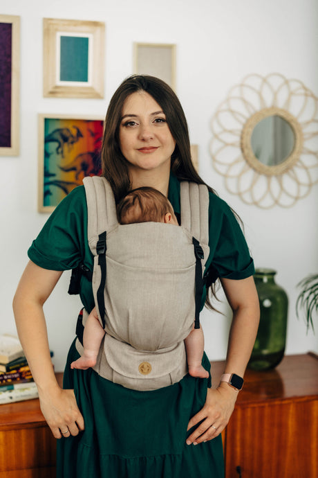 Woman wearing LennyLight baby carrier in Peanut Butter color with a baby on her front.