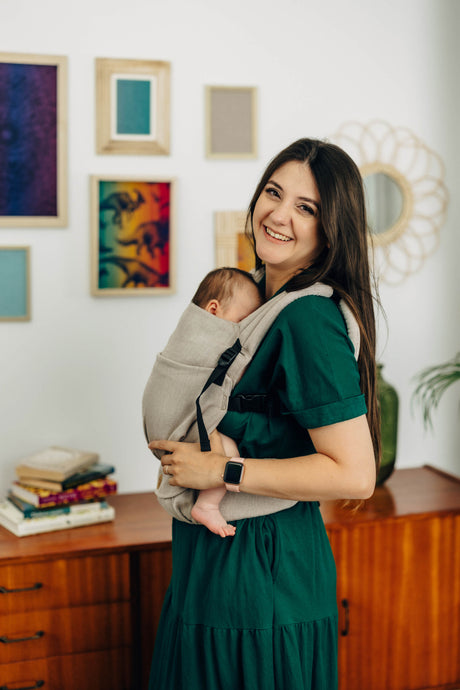 Woman smiling while using the LennyLight baby carrier in Peanut Butter color with a baby comfortably nestled inside.