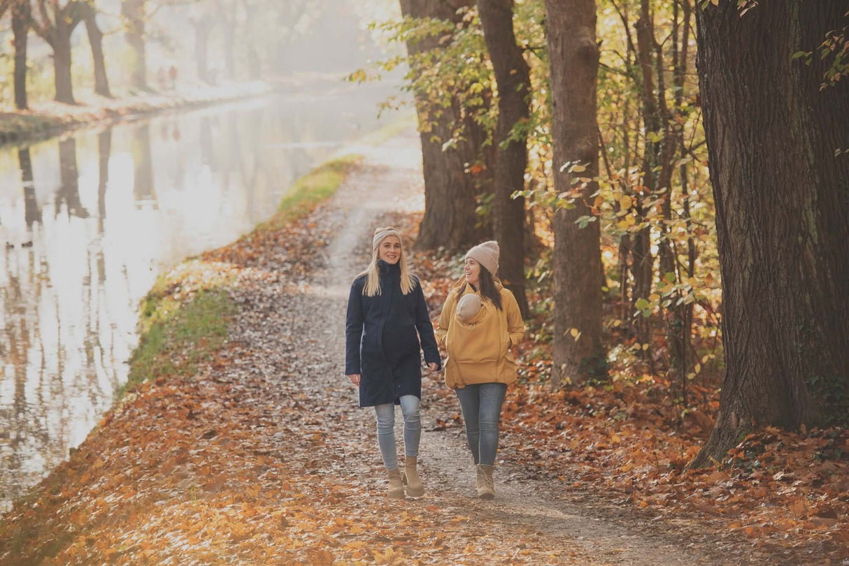 Two women walking along a serene autumn path near a canal, surrounded by colorful leaves | Babymaxi