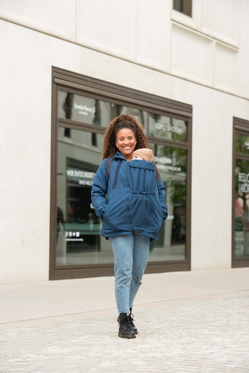 Smiling woman wearing Mamalila Boston Babywearing Jacket - Navy with baby insert on city street | Babymaxi