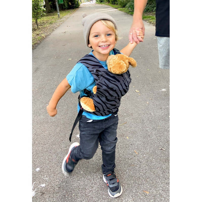 Happy child wearing Manduca Doll Carrier - Zebra with teddy on a walk, made from 100% organic cotton | Babymaxi