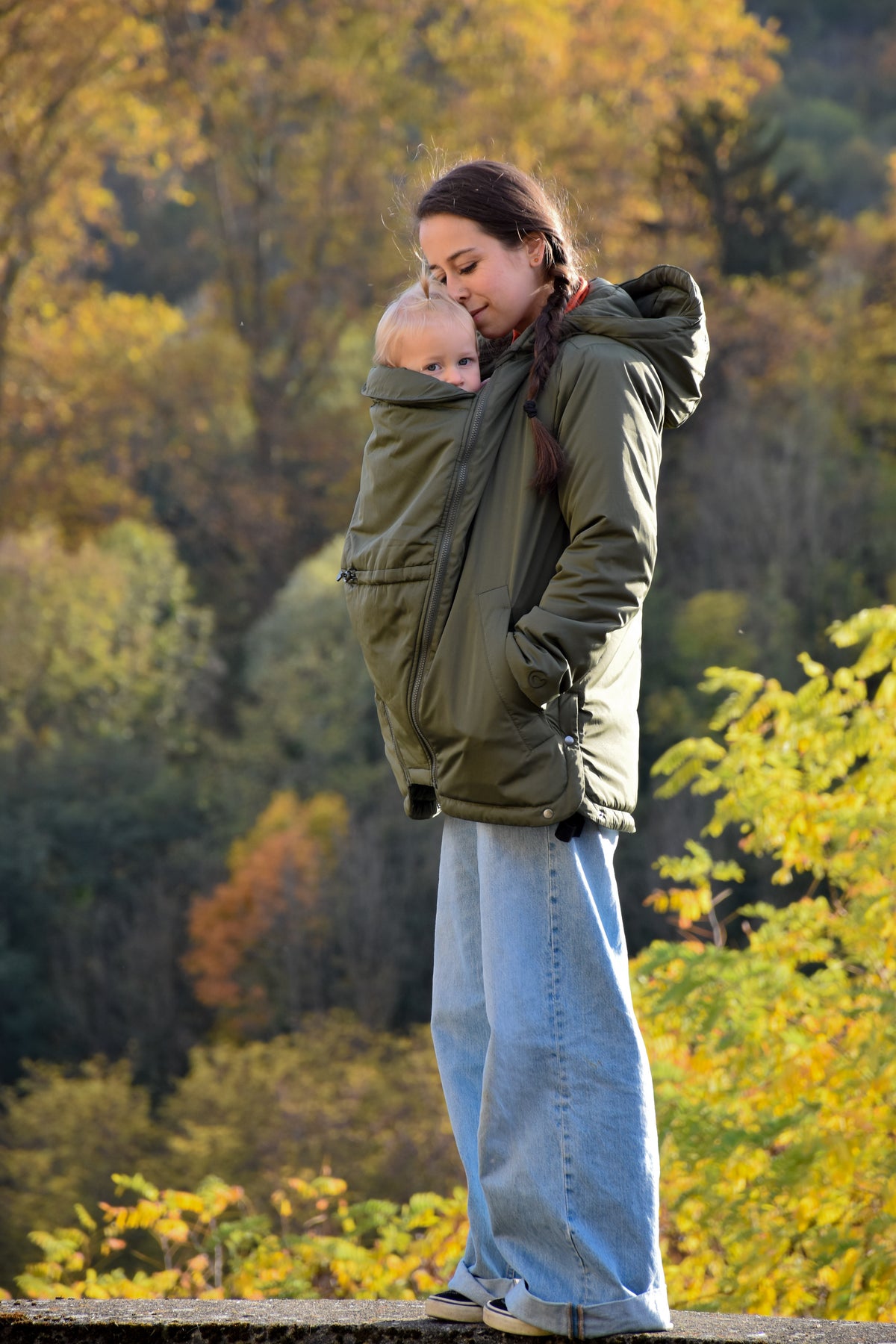 Mamalila Boston Babywearing Jacket Olive, mom wearing baby in carrier jacket on an autumn walk