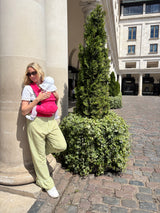Woman wearing Nomad Air Roar baby carrier with infant standing near columns in city plaza