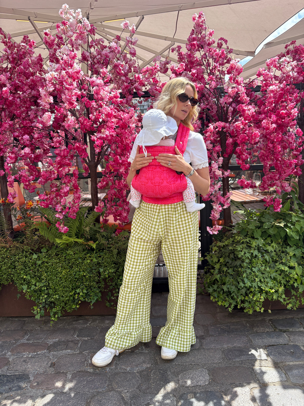 Woman holding infant in Nomad Air Roar baby carrier at outdoor cafe with cherry blossom trees