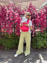 Woman holding infant in Nomad Air Roar baby carrier at outdoor cafe with cherry blossom trees
