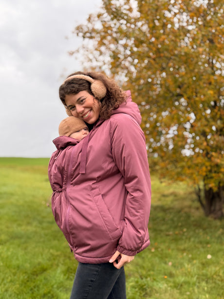 Mamalila Boston Babywearing Jacket Dark Rose, smiling mom carrying baby on front in pink carrier coat outdoors