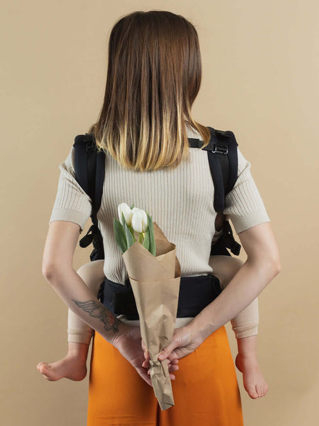 Isara Preschooler (up to 30kg) - Noire baby carrier worn by caregiver with child, featuring chic design and flower bouquet | Babymaxi