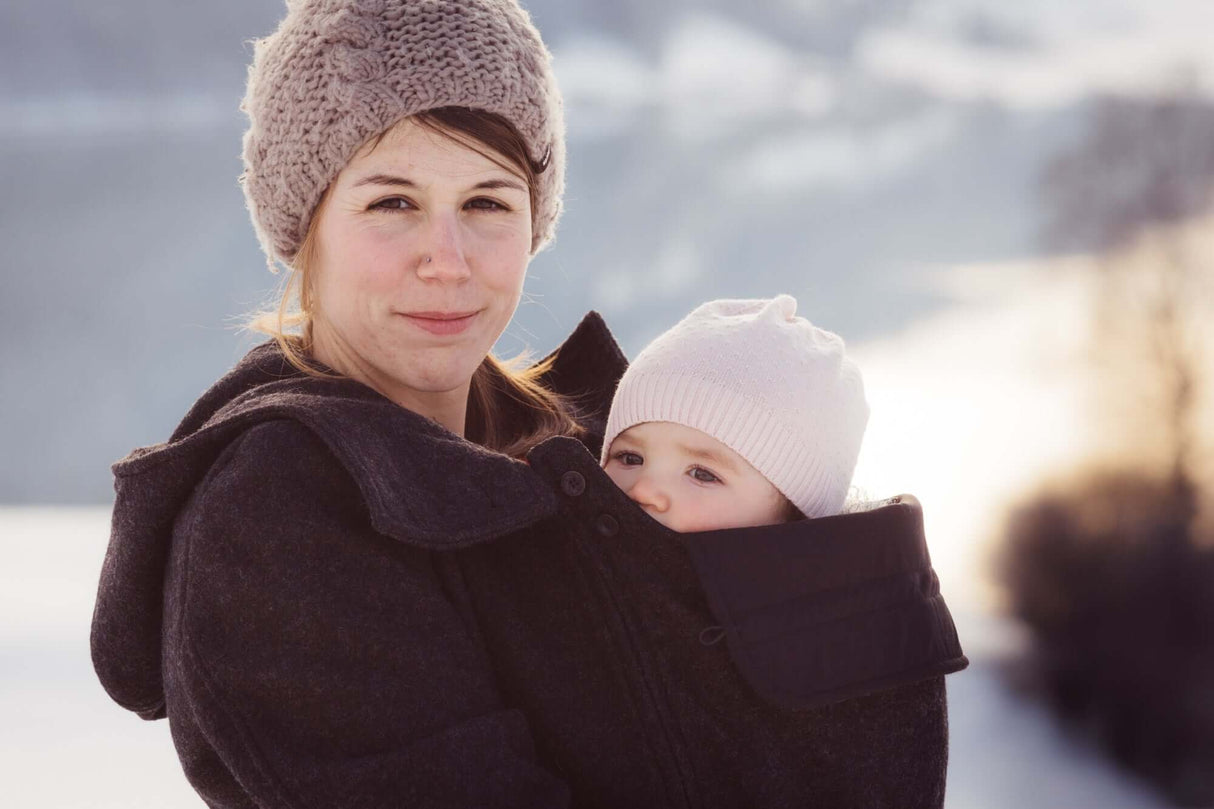 Mamalila Hooded Babywearing Coat Vienna - Anthracite worn by a woman with a baby in snowy landscape | Babymaxi