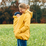 Mamalila Softshell Babywearing Jacket Allrounder - Mustard worn by a mother in a field with her baby | Babymaxi