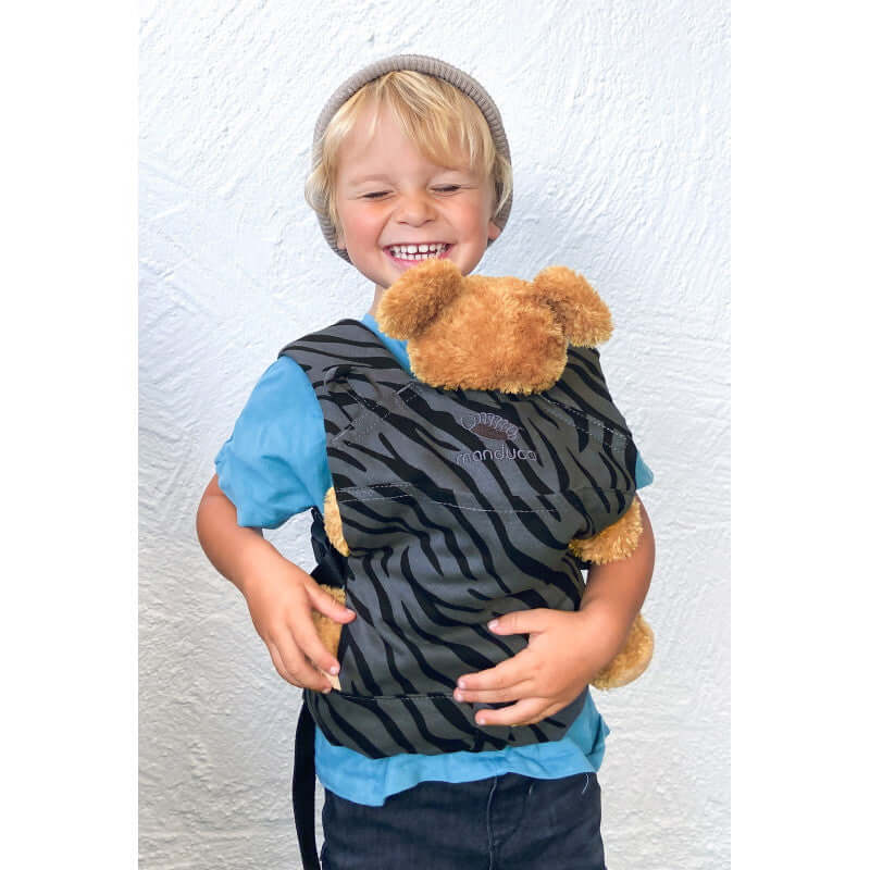 Happy child wearing Manduca Doll Carrier - Zebra with cuddly toy, showcasing organic cotton design | Babymaxi