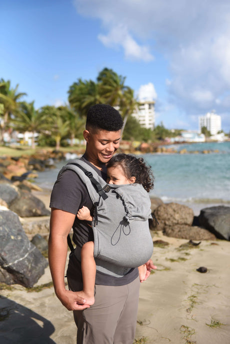 Neko Switch Toddler Carrier - Bold in grey, ergonomically carrying a child on a beach adventure | Babymaxi