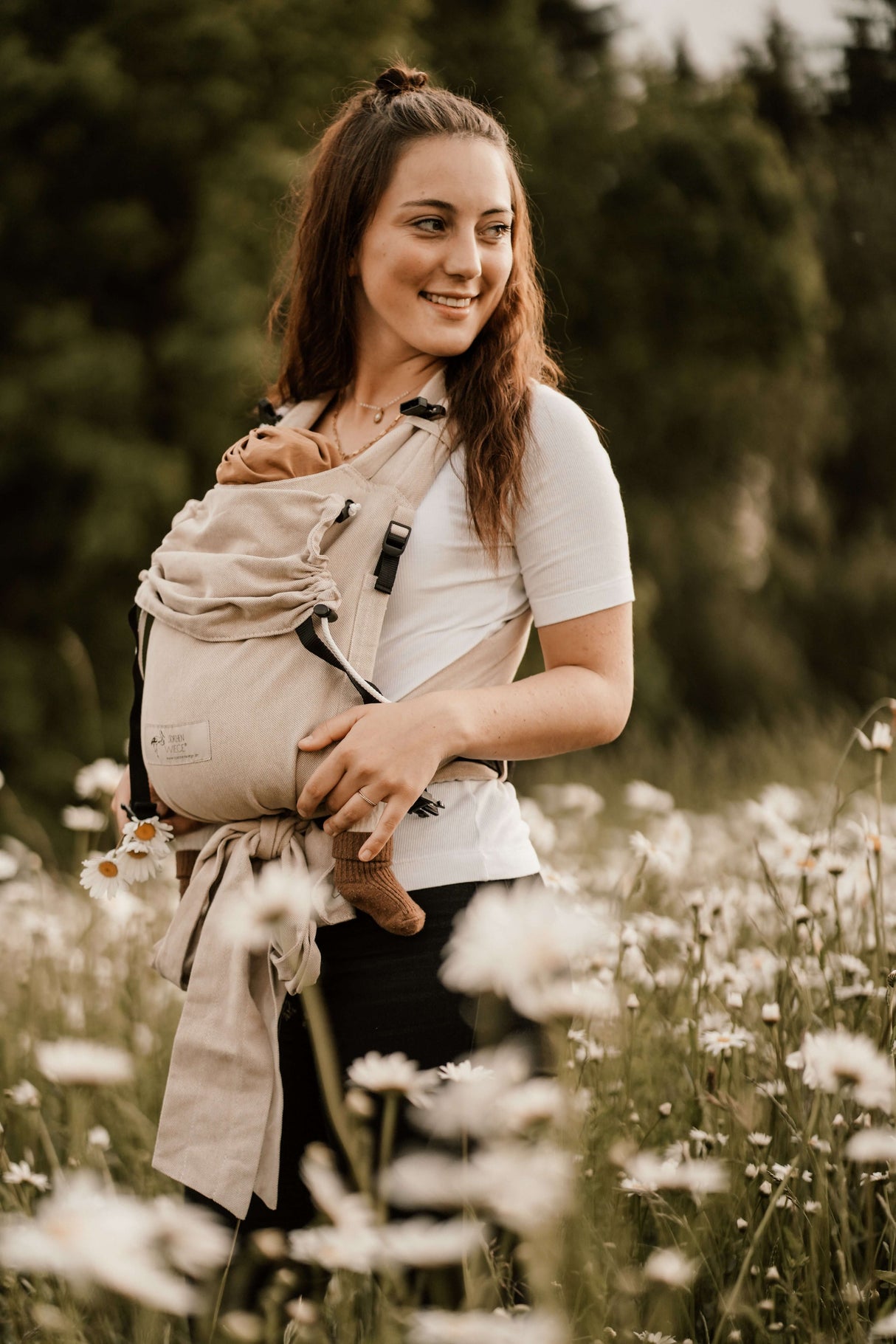 Woman wearing Storchenwiege Talemo Half-Buckle Baby Carrier - Natural with baby in flower field | Babymaxi