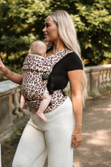 Woman wearing Nomad Air Dusky Leopard baby carrier in profile with infant against garden balustrade