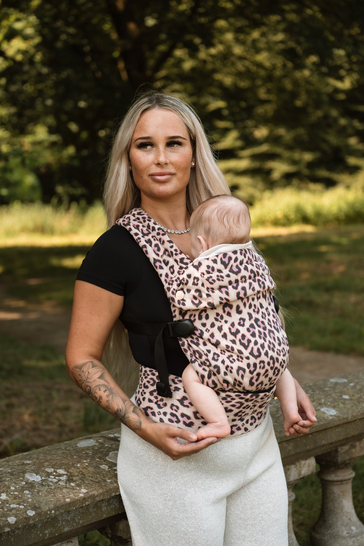 Woman wearing Nomad Air Dusky Leopard baby carrier with infant in wooded park setting